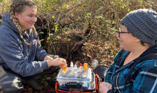 two people smile with small containers of water samples