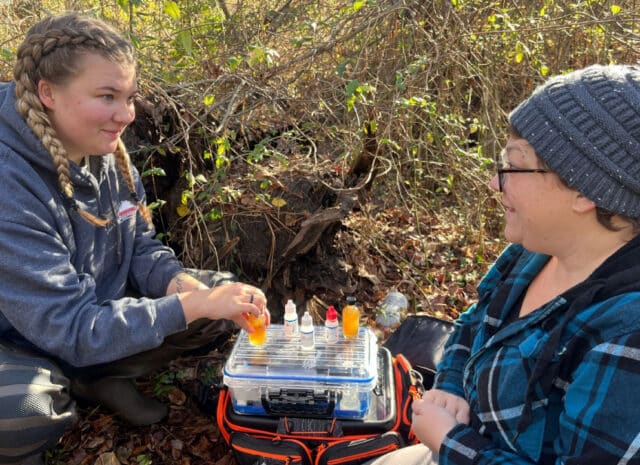 two people smile with small containers of water samples